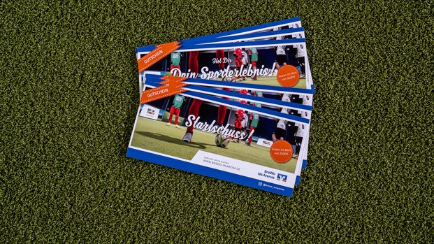 "Starte Dein Fußballabenteuer: Gutschein für ein Sporterlebnis" Ein Stapel von Gutscheinen liegt auf grünem Kunstrasen. Die Gutscheine sind blau umrandet und tragen den Titel "Hol Dir Dein Sporterlebnis" und "Startschuss!" in weißer Schrift. Ein orangener Sticker auf jedem Gutschein zeigt den Wert, entweder 15,00€ oder 20,00€. Im Bildhintergrund ist ein Fußballspiel zu sehen. Die Gutscheine stammen von "BraWo McArenas" und enthalten Informationen zur Buchung.