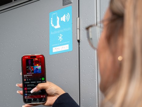 Person streamt Musik über Bluetooth auf dem Smartphone vor einem Audiosystem.