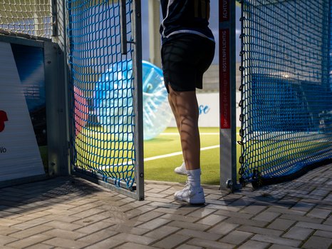 Person verlässt Spielfeld durch ein Tor mit blauen Netzen, Hintergrund zeigt aufgeblasene Kugel.